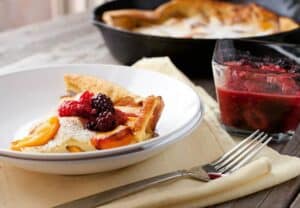 Fresh Peach Dutch Baby: In-season, perfect peaches cooked with a fluffy pancake in a cast iron skillet and served with a quick berry syrup. A perfect late summer breakfast! | macheesmo.com
