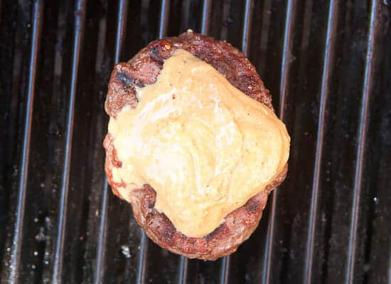 Peanut butter scooped onto burger on the grill.