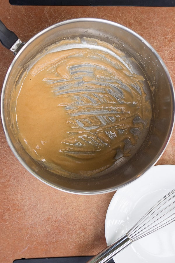 Golden roux in saucepan next to a whisk and plate