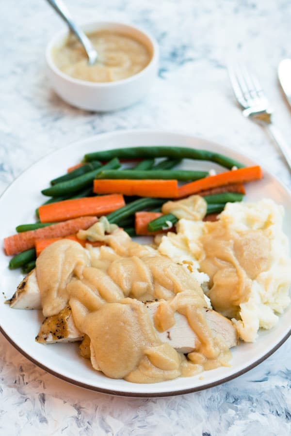 Chicken and mashed potatoes topped with gravy next to beans and carrots