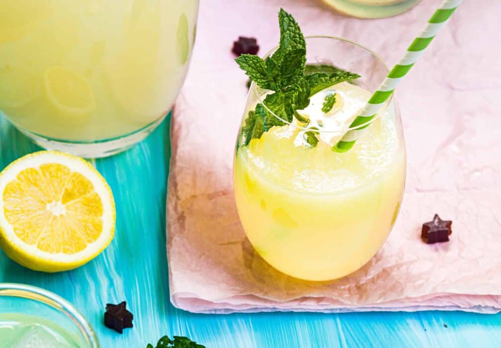A glass of lemonade with a mint garnish and a green-white striped straw