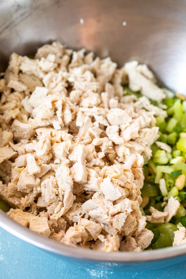 Poached chicken added to salad bowl with crunchy add-ins.