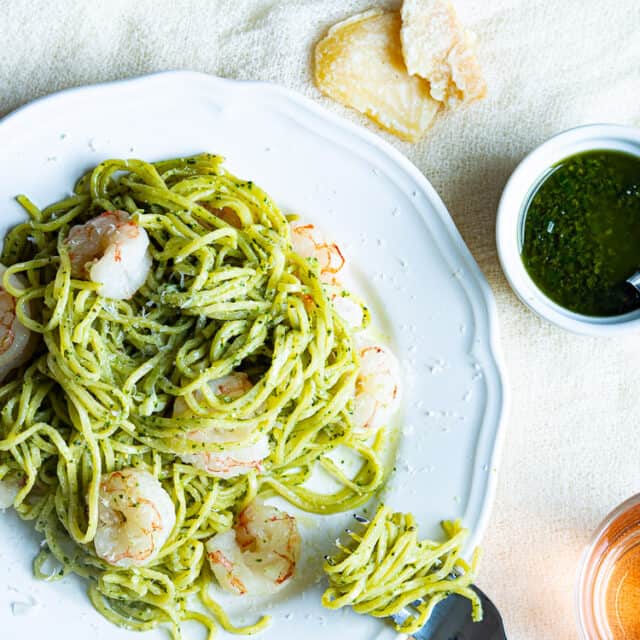 A plate of pasta and shrimp with pesto next to a container of pesto