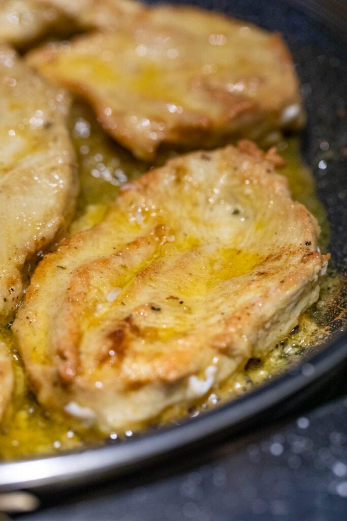 Lightly browned chicken cutlets in a skillet.