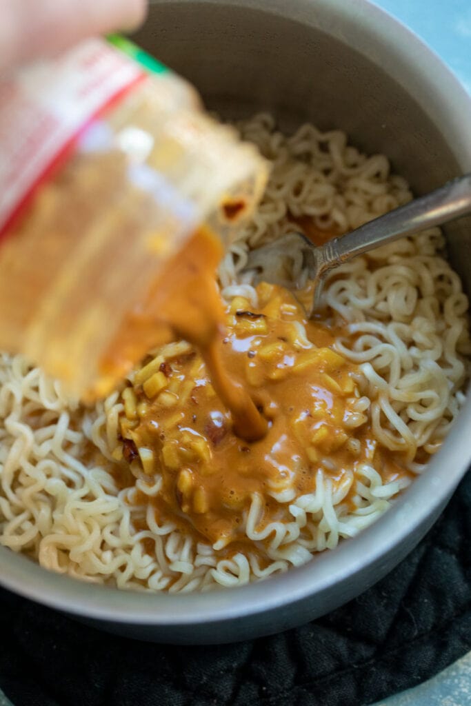 Mixing noodles in the pot with the peanut butter sauce.